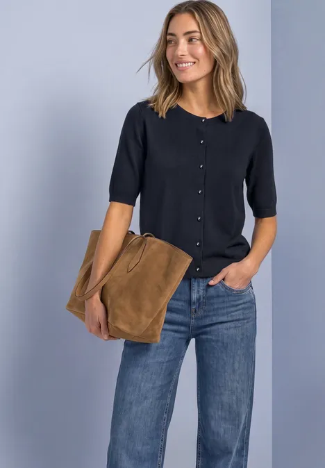 Frau in dunkelblauem Kurzarm-Cardigan, Jeans und brauner Tasche.