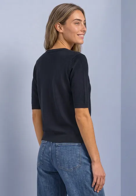 Frau in schwarzem T-Shirt mit halblangen Ärmeln und blauen Jeans, seitliche Rückansicht.