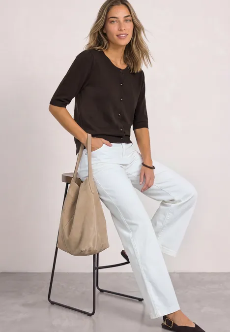 Kurzarm Cardigan mit Rundhals und Knöpfen black coffee Frau mit kurzem dunklen Oberteil, weißen Jeans und Beuteltasche sitzt auf einem Hocker vor hellem Hintergrund.