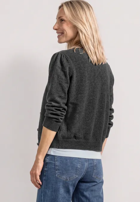 Junge blonde Frau von hinten, blickt über die Schulter, trägt grauen Pullover mit weißen Bündchen und Jeans.