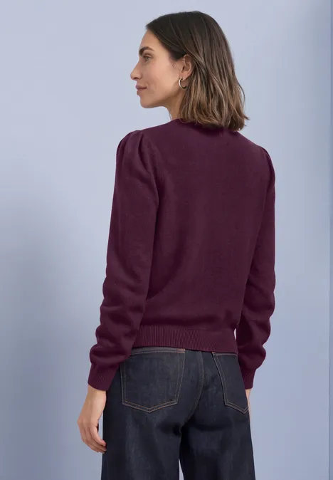 Langarm Cardigan mit Rundhals und Knöpfen berry maroon mel. Eine Frau in Profilansicht trägt einen dunkelroten Pullover und dunkle Jeans vor neutralem Hintergrund.