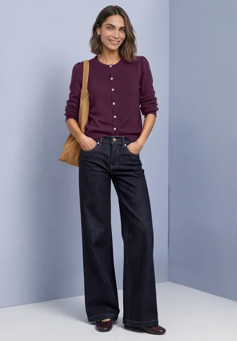 Langarm Cardigan mit Rundhals und Knöpfen berry maroon mel. Eine lächelnde Frau in lila Strickjacke, weiten Jeans und Tasche vor neutralem Hintergrund.