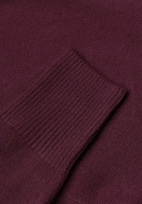 Nahaufnahme eines weinroten Strickpulloverärmels mit Rippenstrickbündchen.