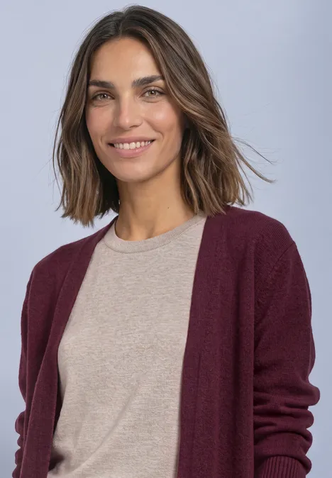 Eine junge Frau mit schulterlangem braunem Haar, lächelnd, trägt beiges Shirt und bordeauxroten Cardigan.