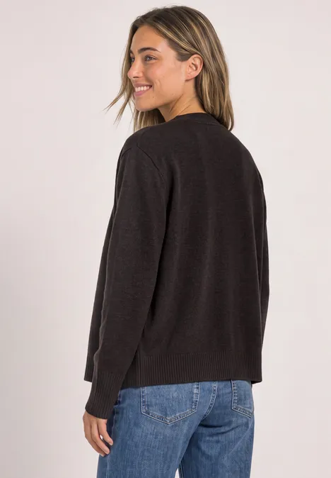 Frau im schwarzen Cardigan und blauen Jeans, von hinten fotografiert und über die Schulter blickend.