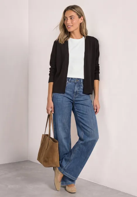 Frau in weißem T-Shirt, schwarzer Jacke, weiten Jeans, beigen Schuhen und brauner Tasche