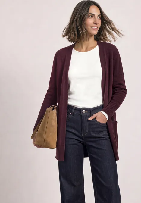 Femme en gilet bordeaux, t-shirt blanc, jean foncé et sac beige, sourire naturel, allure décontractée.