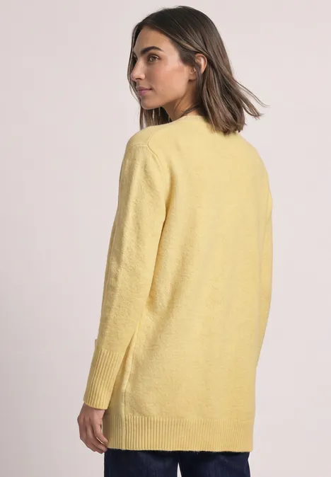 Langarm Cardigan mit aufgesetzten Taschen sunbeam yellow mel. Frau in gelbem Cardigan blickt über die Schulter, Rückansicht mit dezentem Profil.