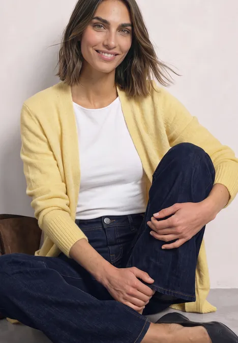 Langarm Cardigan mit aufgesetzten Taschen sunbeam yellow mel. Lächelnde Frau in gelbem Cardigan, weißem T-Shirt und dunklen Jeans sitzt entspannt am Boden.