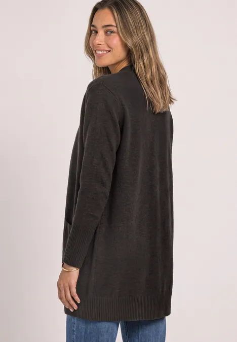 Jeune femme de profil portant un long cardigan marron foncé et souriant à la caméra.