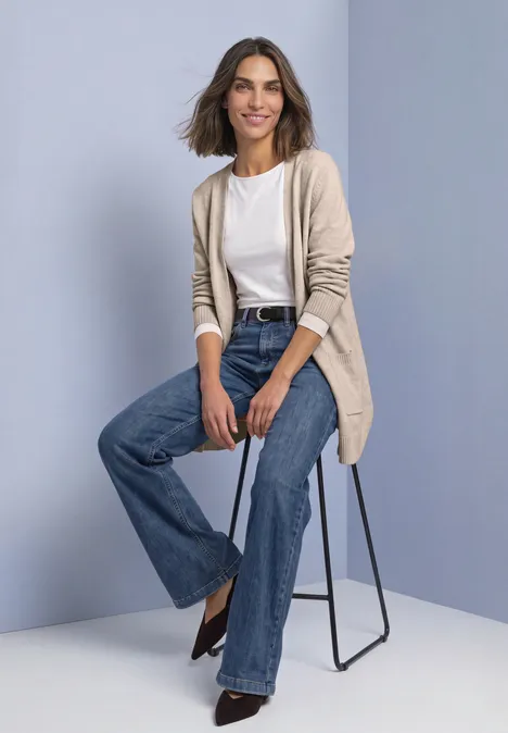 Langarm Cardigan mit aufgesetzten Taschen clay sand mel. Frau auf Hocker in beigem Cardigan, weißem Top, weiten Jeans und schwarzen Schuhen vor neutralem Hintergrund.