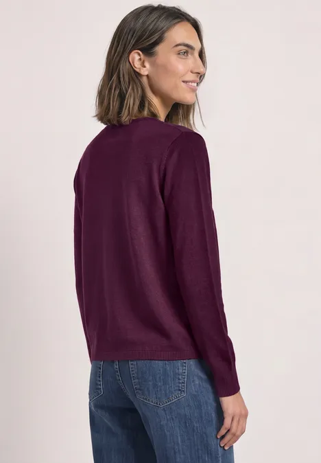 Kardigan z rozpinanym dekoltem w jednolitym kolorze berry maroon Kobieta w ciemnofioletowym swetrze z długimi rękawami i dżinsach, spogląda przez ramię, proste studio.