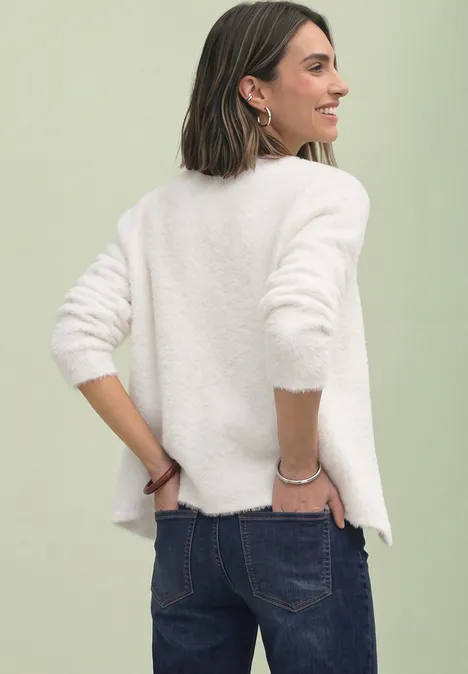 Cardigan à manches longues, col en V et boutons off white Frau mit schulterlangen Haaren trägt weißen Pullover und Jeans, lächelt seitlich in die Kamera.