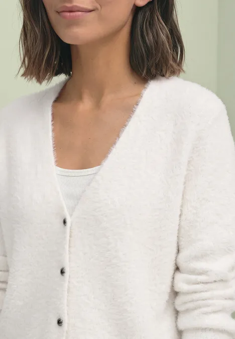 Cardigan à manches longues, col en V et boutons off white Frau in weißer flauschiger Strickjacke und weißem Top, Close-up auf Oberkörper und Arme.