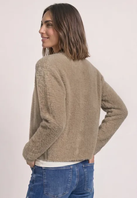 Een vrouw in beige teddyjack en spijkerbroek, schuin van achteren gefotografeerd, glimlacht over haar schouder.