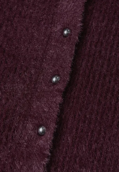 Nahaufnahme eines weinroten, flauschigen Strickcardigans mit Rippenstruktur und glänzenden Knöpfen.