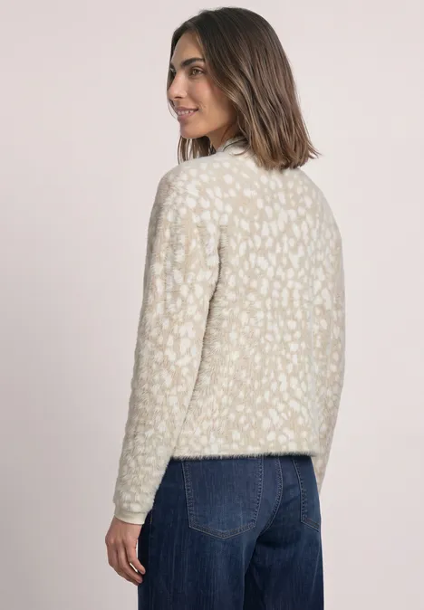 Frau steht im Profil, trägt gemusterten Creme-Pullover und blaue Jeans.