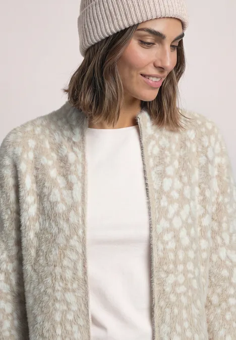 Frau mit hellgrauer Strickmütze und flauschigem, creme-beigem Leoparden-Cardigan über weißem Shirt.