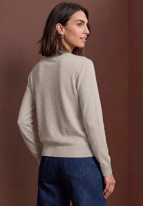 Cardigan mit Rundhals und Knopfleiste clay sand mel. Frau in beigem Pullover und blauen Jeans, von hinten vor braunem Hintergrund
