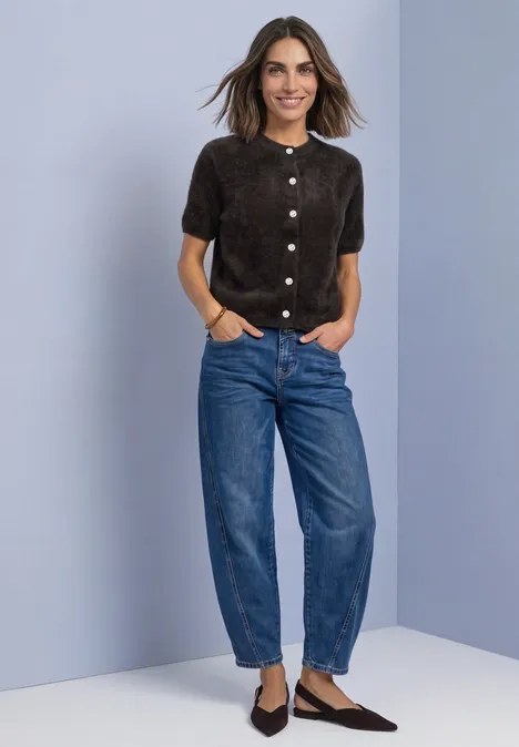 Vrouw in bruine korte blouse, wijde spijkerbroek en puntige schoenen voor lila achtergrond.