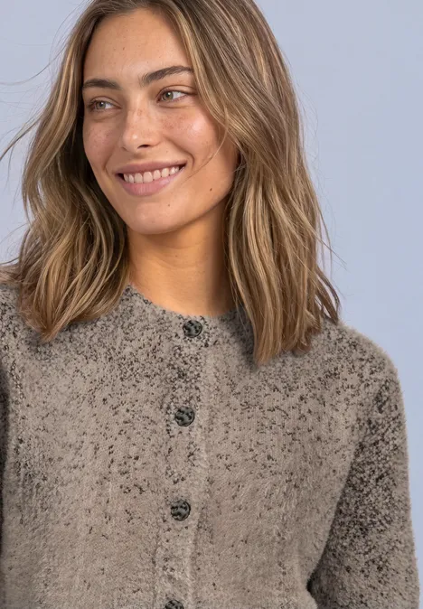 Eine Frau mit flauschigem Knopf-Pullover lächelt, helle Haare, entspannte Haltung.