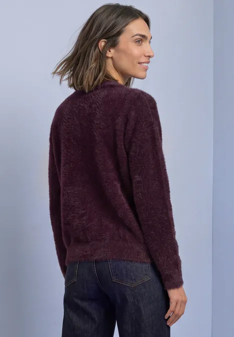 Frau in flauschigem lila Pullover und Jeans, von hinten seitlich fotografiert.
