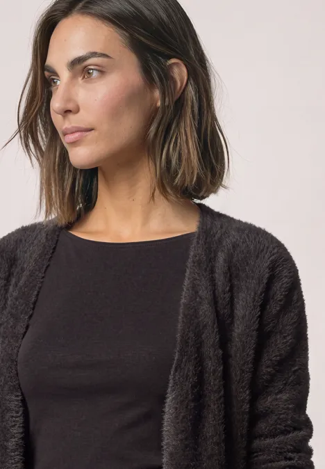 Eine Frau mit dunklem, flauschigem Cardigan und schwarzem Oberteil schaut zur Seite.
