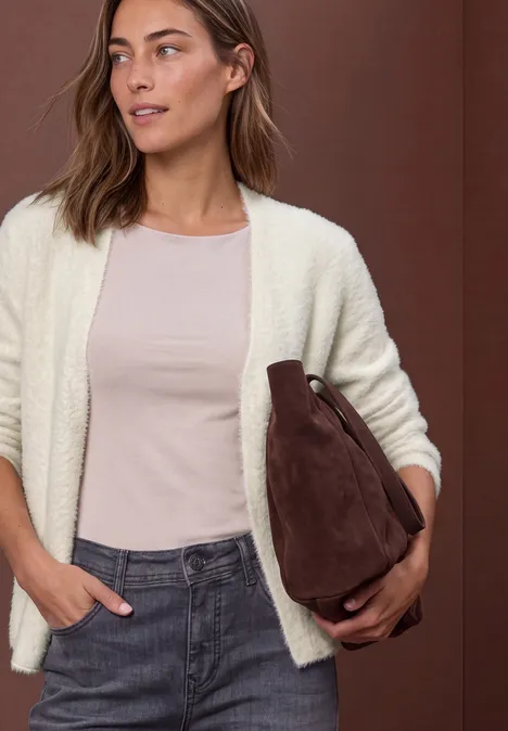 Frau in heller Strickjacke, rosa Shirt und Jeans hält eine braune Tasche unter dem Arm.