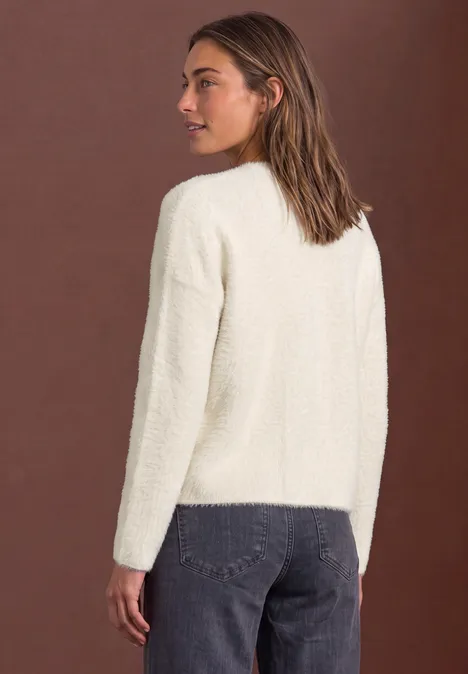 Frau in cremeweißem Kuschelsweater und Jeans vor braunem Hintergrund