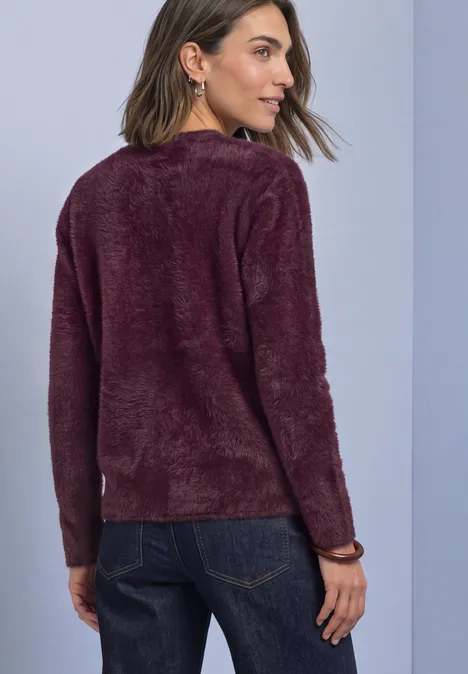Frau von hinten in dunkelblauer Jeans und beerenfarbenem, flauschigem Pullover vor neutralem Hintergrund.