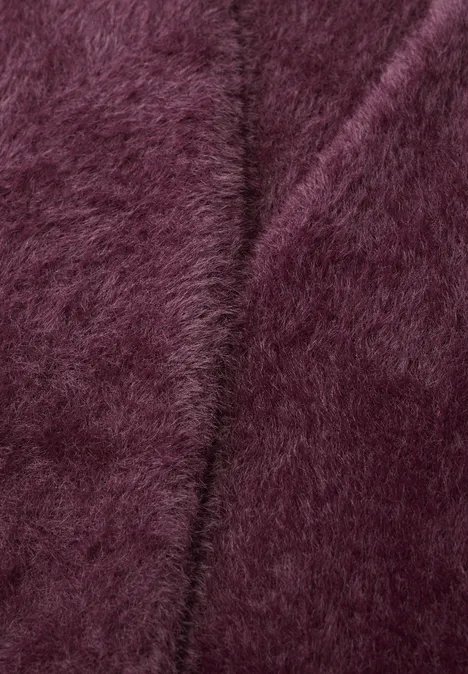 Nahaufnahme eines flauschigen, burgunderfarbenen Stoffes mit weicher, pelziger Oberfläche.