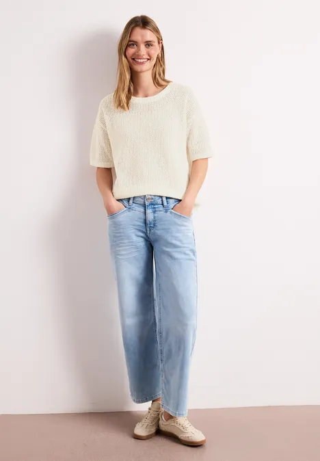 Trui met korte mouwen en netstructuur soft beige Persoon draagt crèmekleurige korte trui en wijde lichtblauwe jeans, staat voor witte muur met handen in zakken.