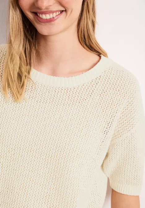 Trui met korte mouwen en netstructuur soft beige Close-up van een glimlachende vrouw in een crème-kleurige, losgebreide trui met korte mouwen.