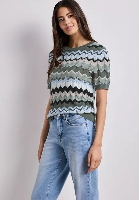 Vrouw draagt kleurrijk zigzagshirt met korte mouwen en een spijkerbroek.