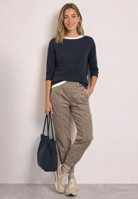 Vrouw in donkerblauwe trui, wit shirt, beige cargobroek, sneakers en bijpassende tas