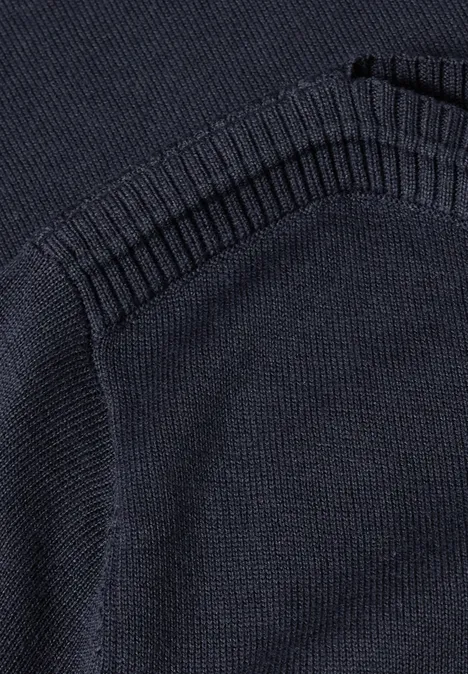 Close-up van een donkerblauwe gebreide trui met opgestikte zak en geribbelde boorden.