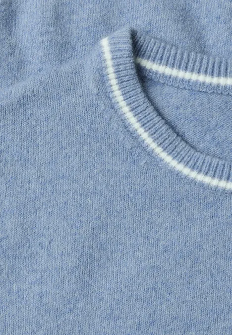 Zbliżenie na jasnoniebieski sweter z dzianiny z białą lamówką przy okrągłym dekolcie.