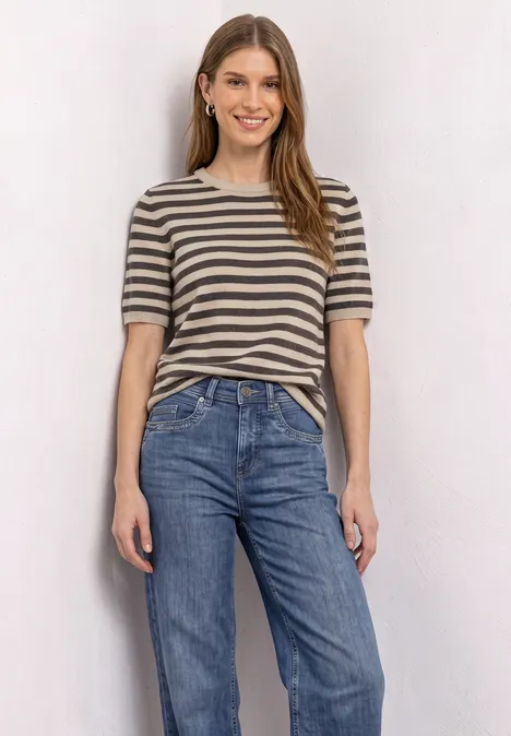 Eine junge Frau trägt ein gestreiftes T-Shirt und Jeans, sie lächelt entspannt.