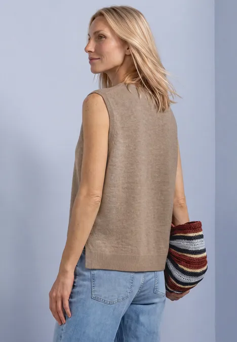 Pullunder mit V-Neck in Unifarbe sanded amber mel. Eine blonde Frau trägt eine beige, ärmellose Strickweste, blaue Jeans und hält eine bunte, gestreifte Tasche.
