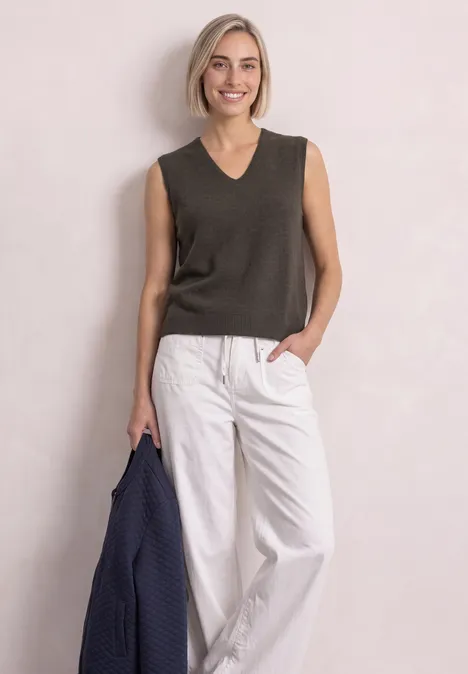 Pullunder mit V-Neck in Unifarbe black coffee mel. Eine lächelnde Frau in dunkelgrauem Top und weißen Hosen hält eine blaue Jacke.