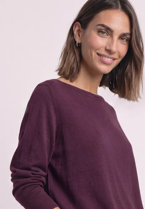 Porträt einer lächelnden Frau in violettem Pullover vor hellem Hintergrund.