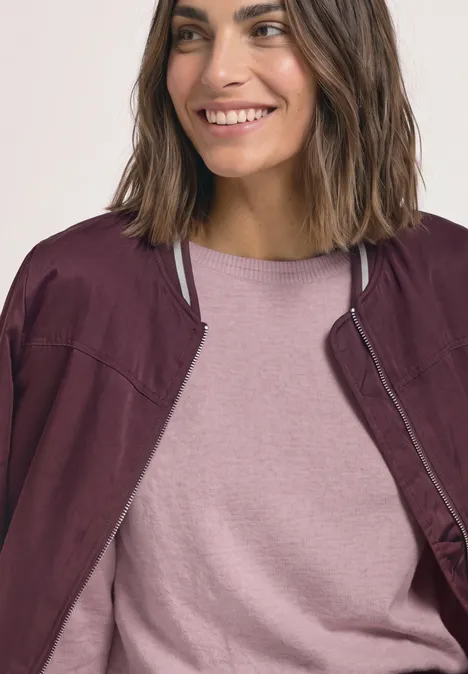 Sweter Basic z dekoltem w łódkę quiet rose mel. Uśmiechnięta kobieta z półdługimi włosami ma na sobie różowy t-shirt i bordową kurtkę.