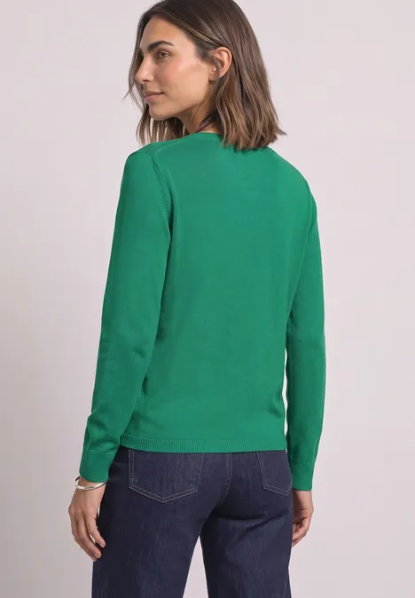 Frau von hinten in grünem Langarmshirt und Jeans, Kopf zur Seite gedreht.