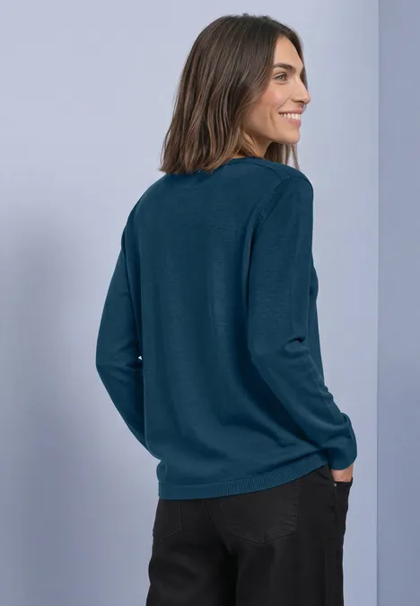 Basic Pullover mit U-Boot-Ausschnitt blue petrol Frau von hinten mit dunkelgrünem Langarmshirt und schwarzer Hose, lächelt seitlich vor hellem Hintergrund.