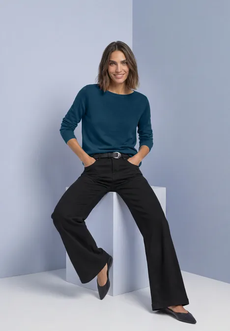Basic Pullover mit U-Boot-Ausschnitt blue petrol Frau in blaugrünem Pullover und schwarzen, weiten Hosen, lächelnd in minimalistischem Raum posierend.