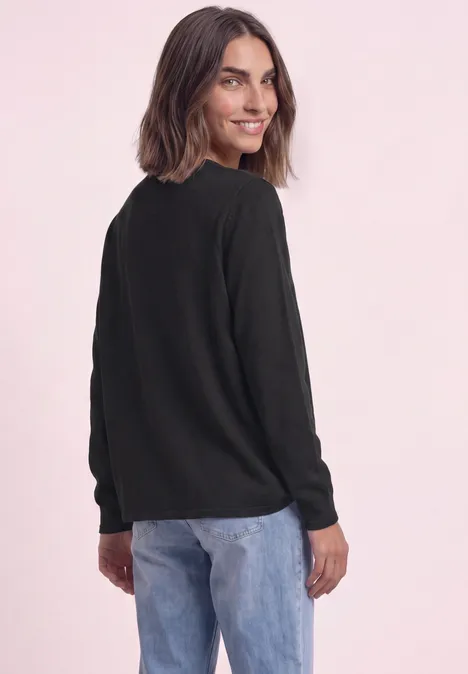 Eine Frau in schwarzem Pullover und blauer Jeans schaut über ihre Schulter.