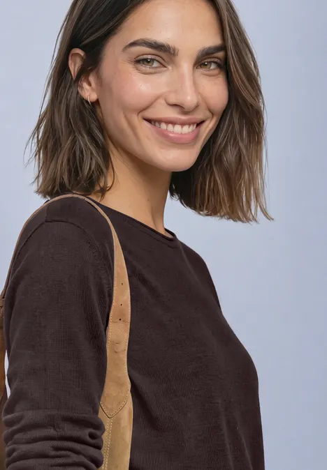 Pullover mit Rundhals und Rollkanten ruby vine Lächelnde Frau mit braunen Haaren in schwarzem Pullover und brauner Umhängetasche vor hellem Hintergrund.