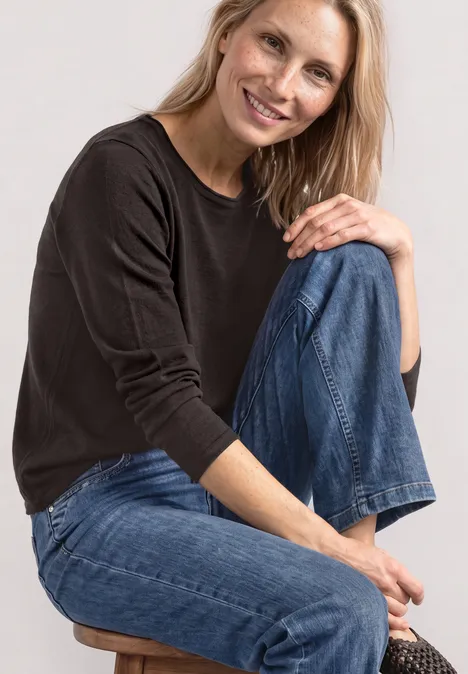 Pullover mit Rundhals und Rollkanten black coffee Eine lächelnde Frau in schwarzem Pullover und blauen Jeans sitzt auf einem Hocker.