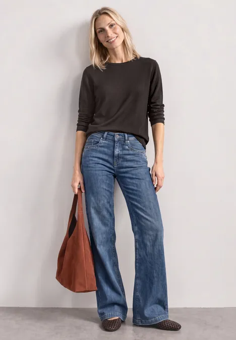 Pullover mit Rundhals und Rollkanten black coffee Frau mit schwarzem Pullover, weiten blauen Jeans und brauner Tasche lächelt vor neutralem Hintergrund.