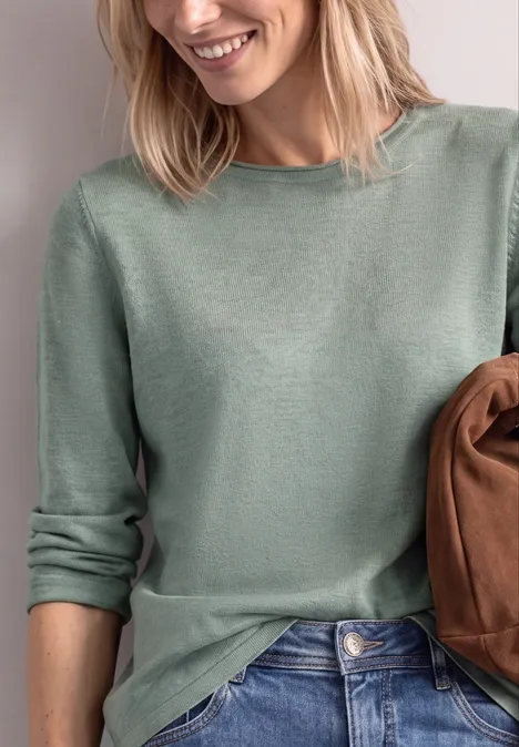 Frau trägt grünen Pullover und hält eine braune Tasche.